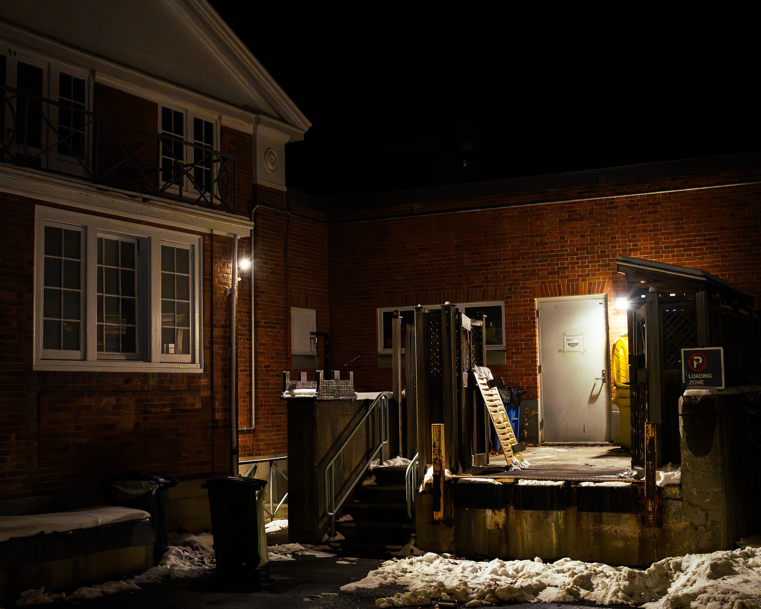 The service yard at night: brick wall, steel doors, a metal stair, packed snow underfoot.