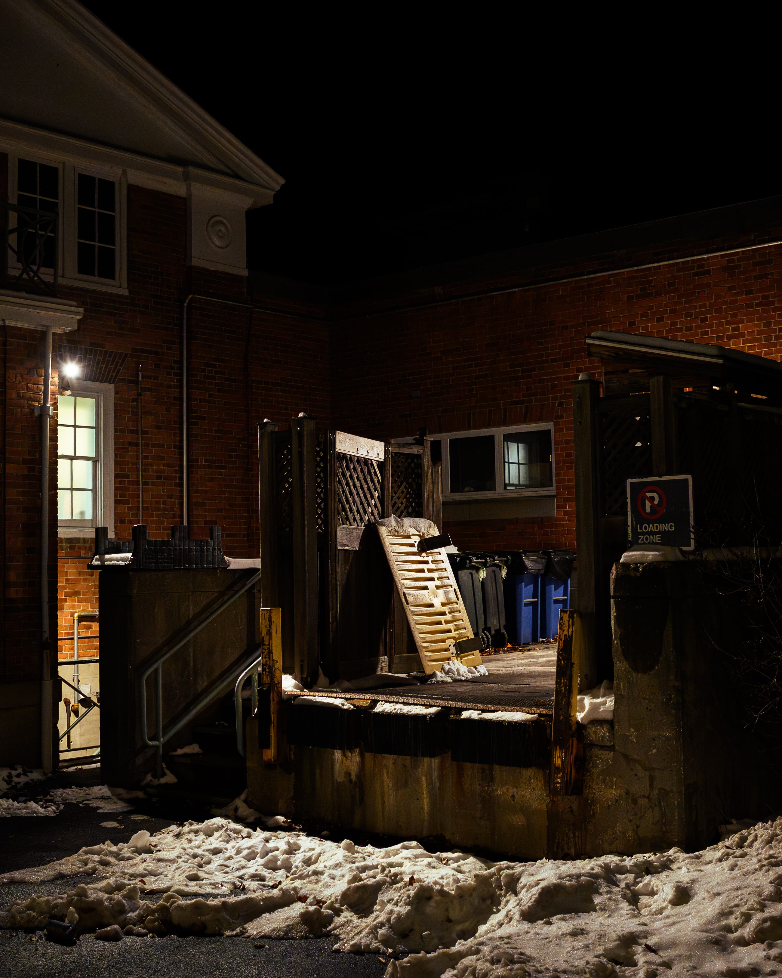 Wider view of the yard, air-conditioning units ranked along the wall, a parking sign above.