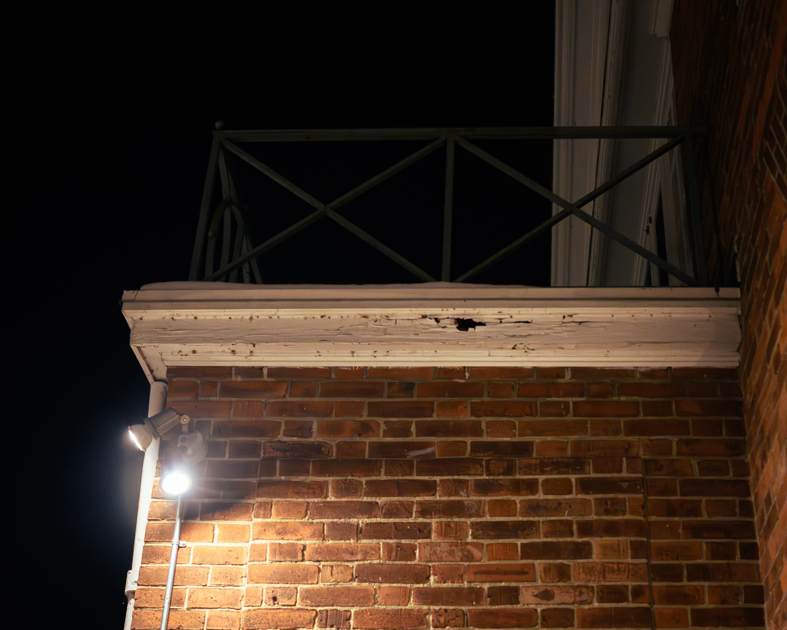 A brick corner under a security light at night, the beam raking across the coursing.