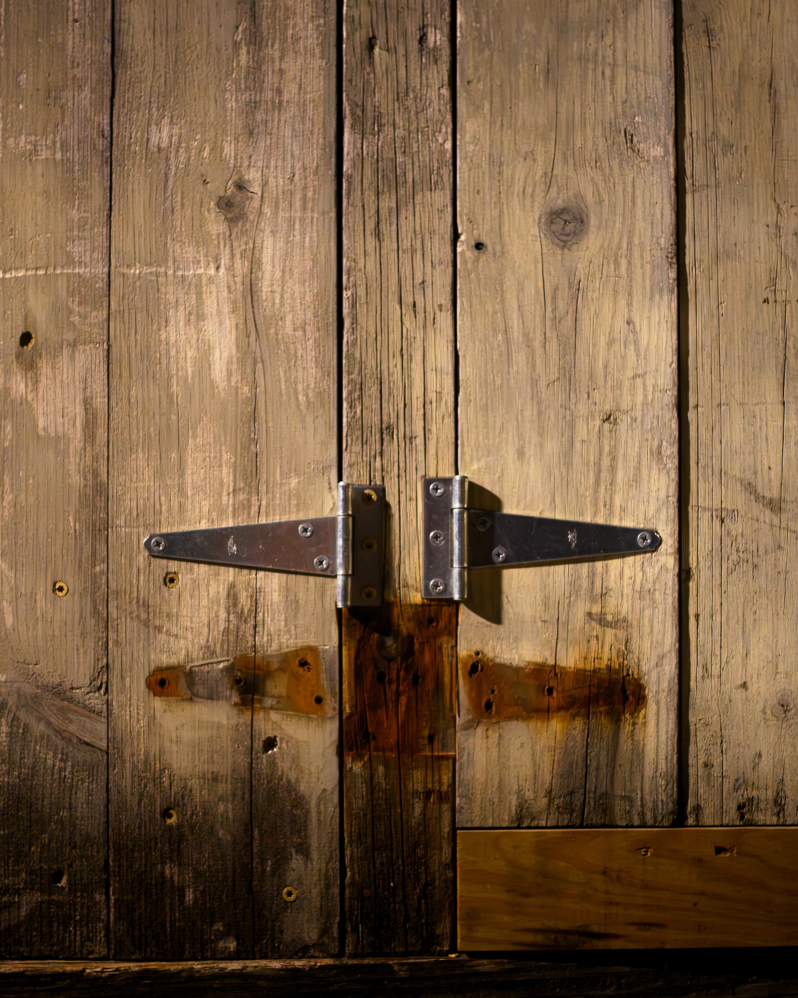 Weathered timber doors held shut by a plain steel strap hinge, rust bleeding down the grain.