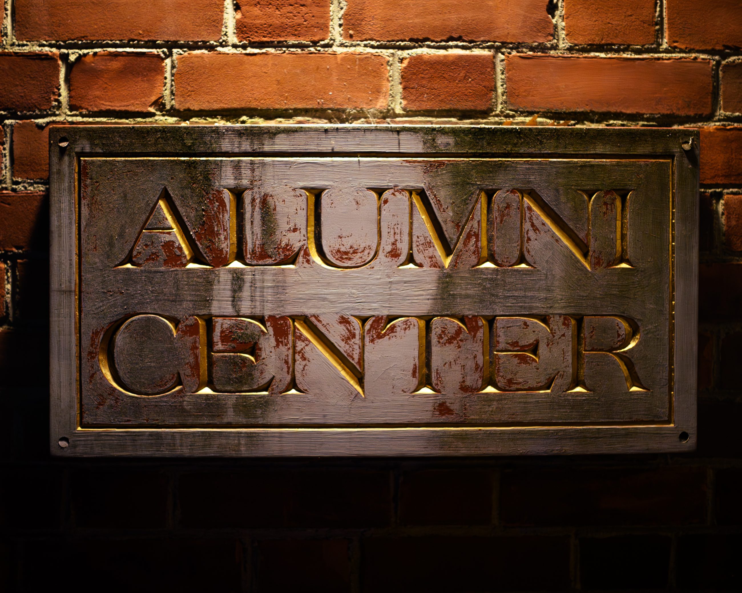 A brass plaque reading ALUMNI CENTER, mounted on brick, photographed at night in the service area.