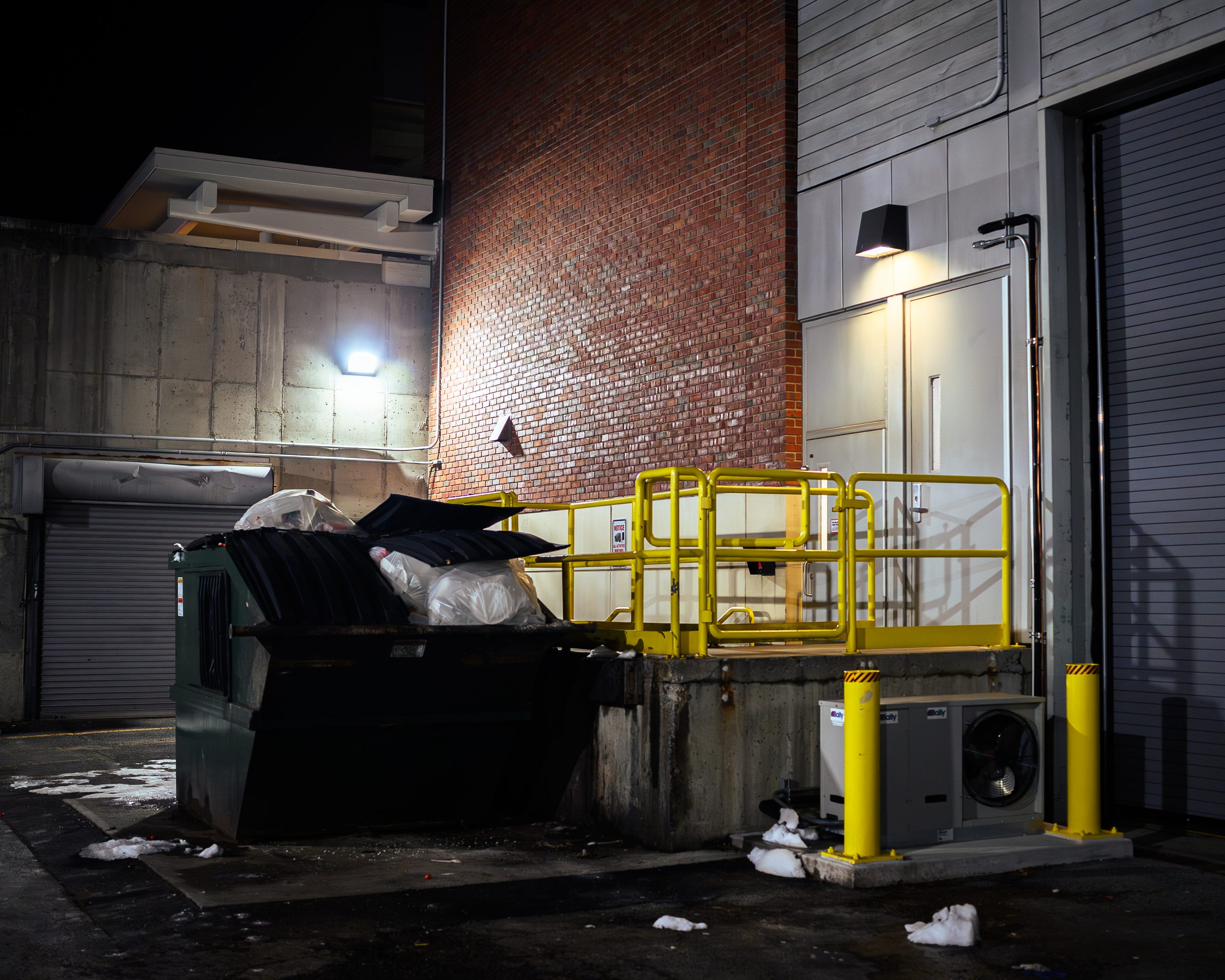 The dock from the other side, yellow safety railings, litter across the ground, a dumpster standing open.