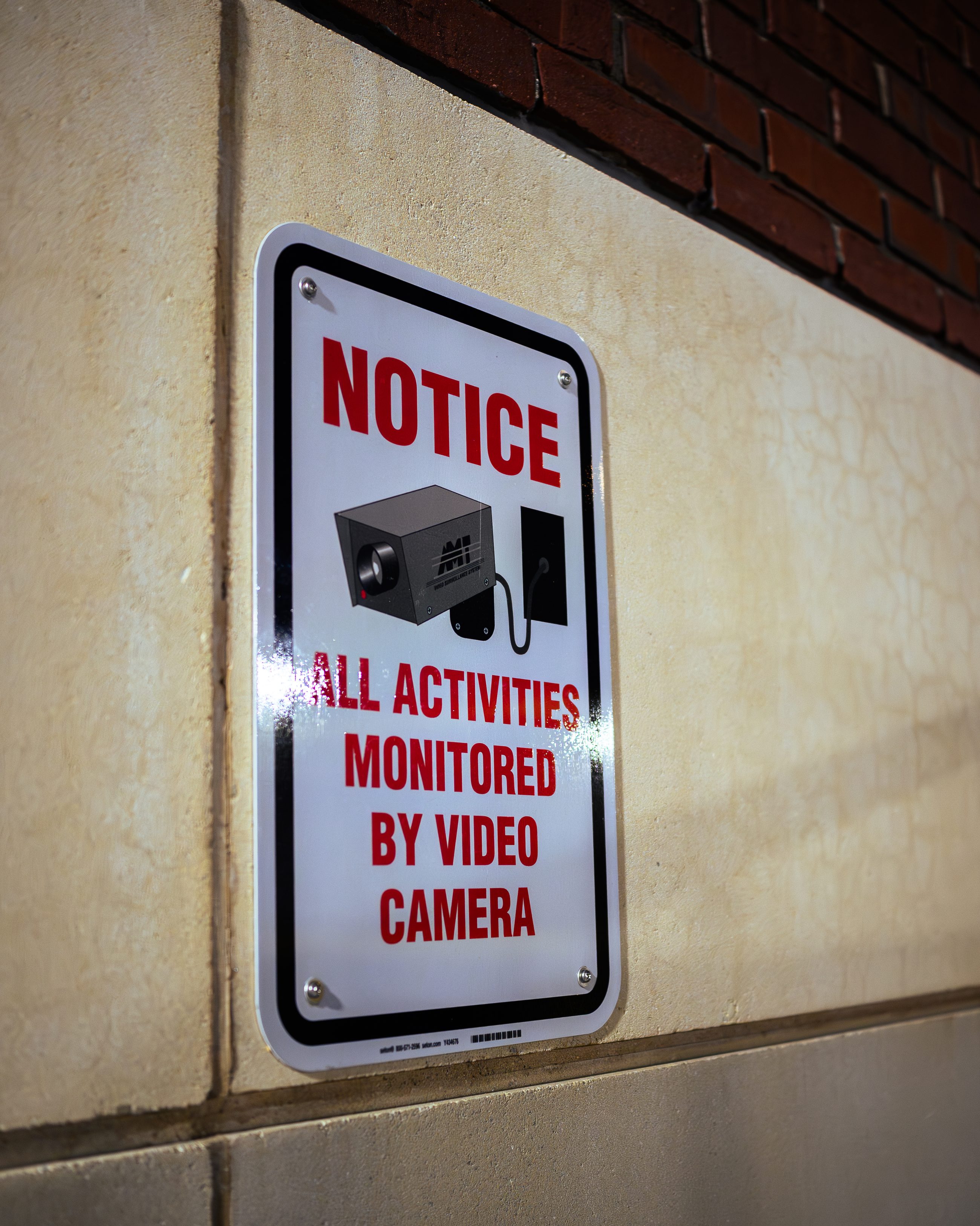 A notice on the wall: ALL ACTIVITIES MONITORED BY VIDEO CAMERA, in red, above a drawing of two cameras.