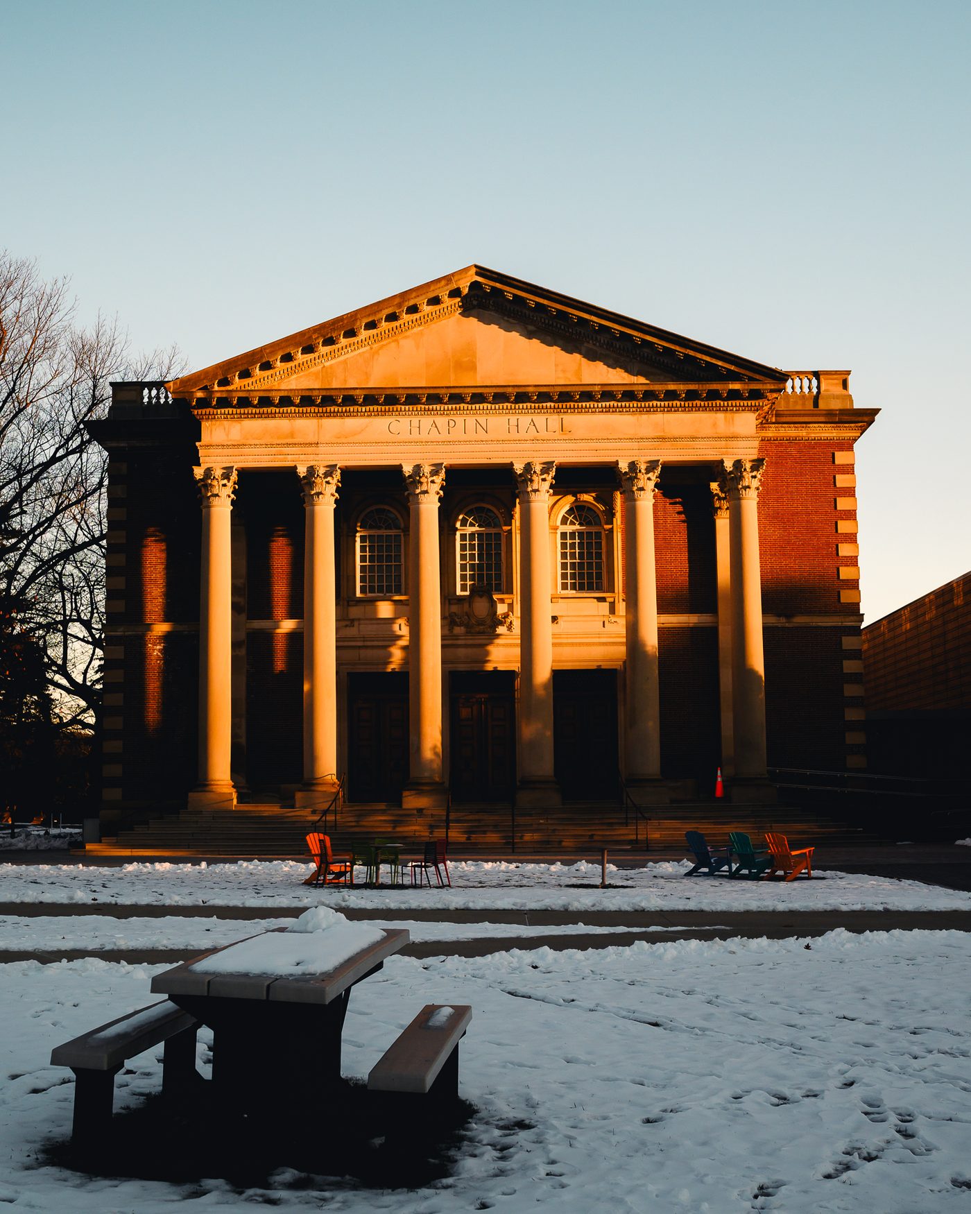 Chapin Hall's columned portico lit orange by low winter sun, snow across the ground, a picnic table in shadow.