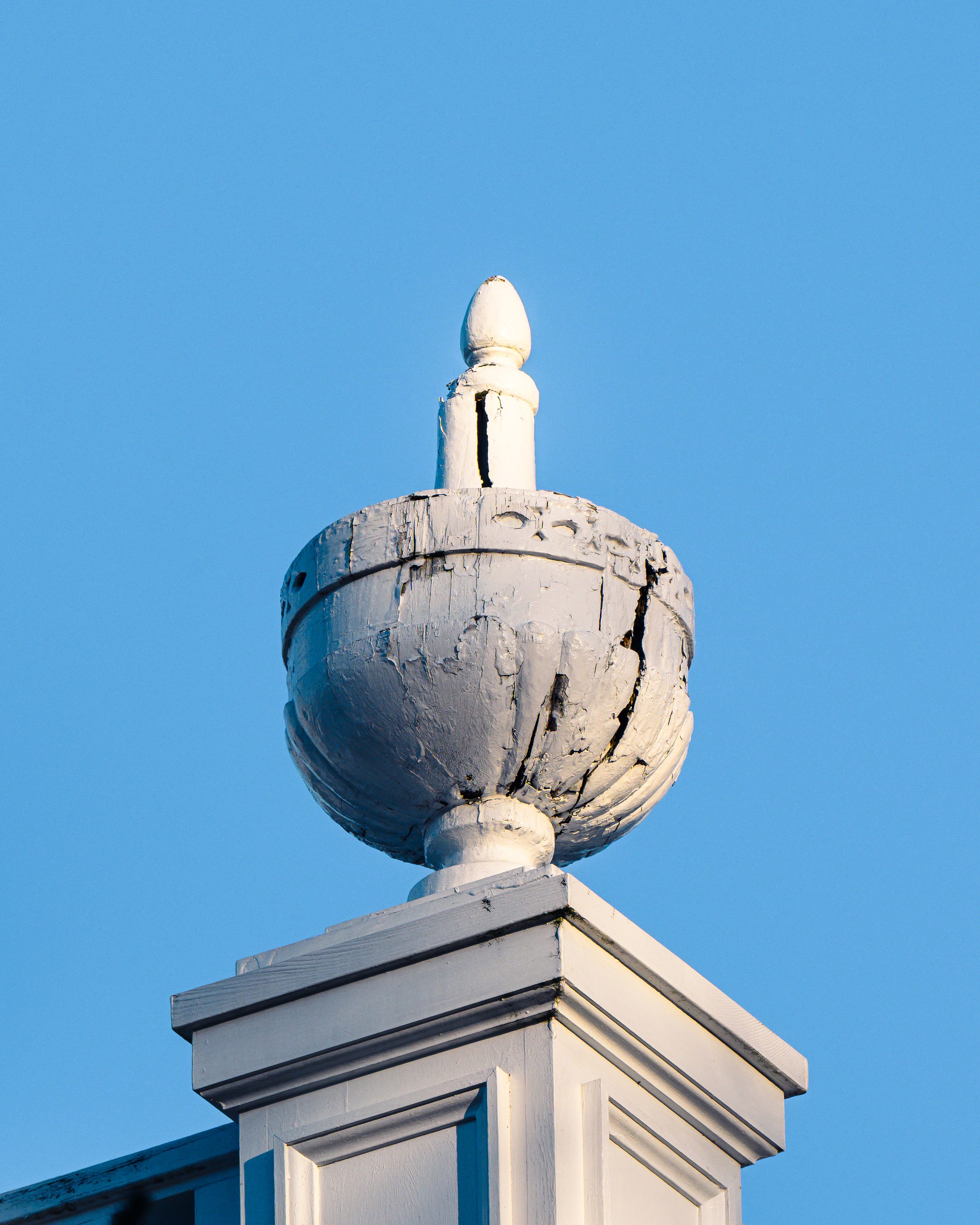 A weathered stone finial on a gatepost, isolated against flat blue sky.