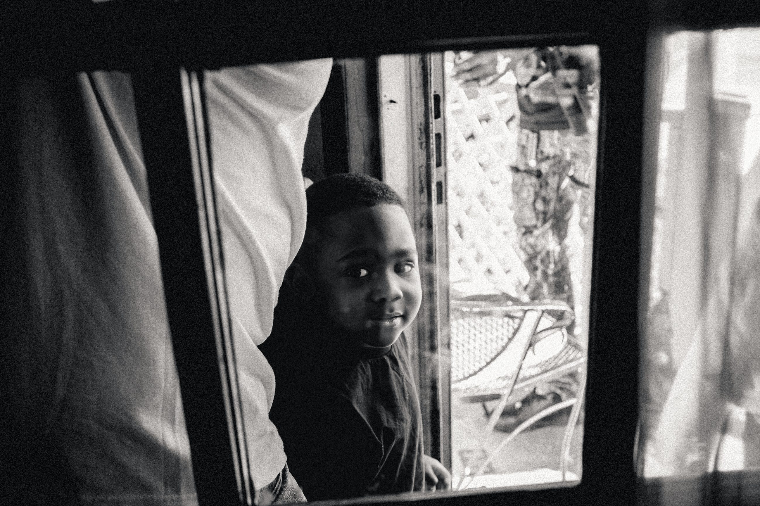 A boy's face at a window, curtains drawn back around him.
