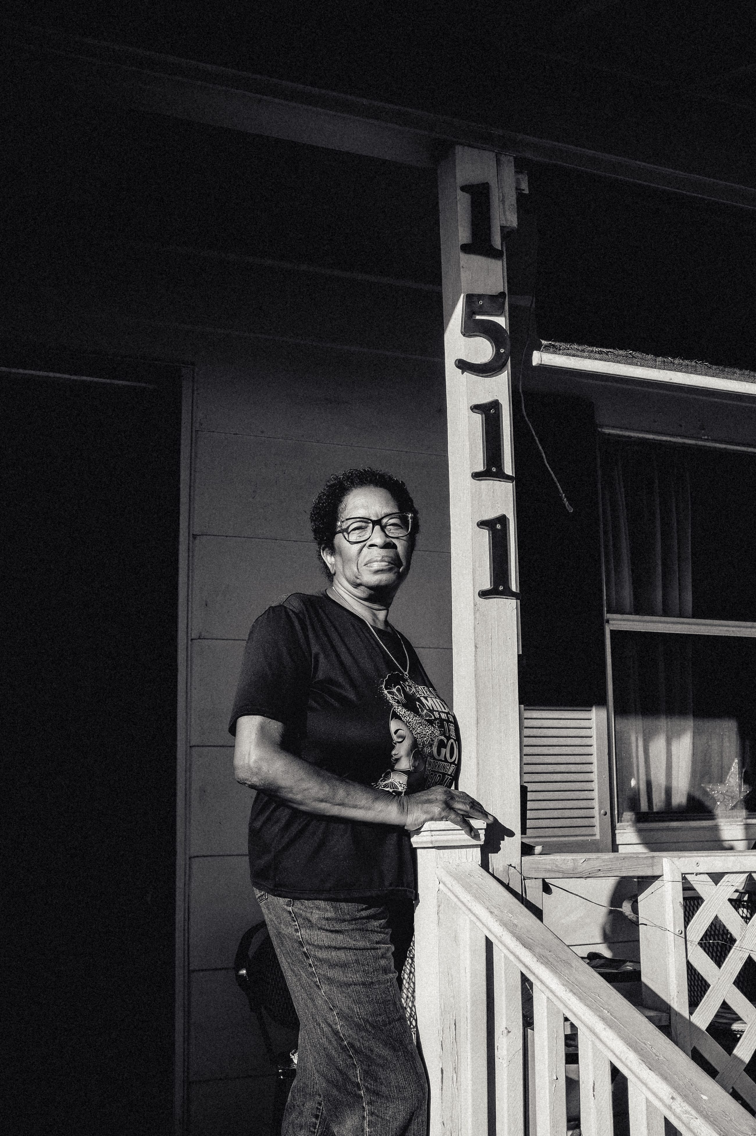 A woman standing on her porch after dark, beside the house number 1511.