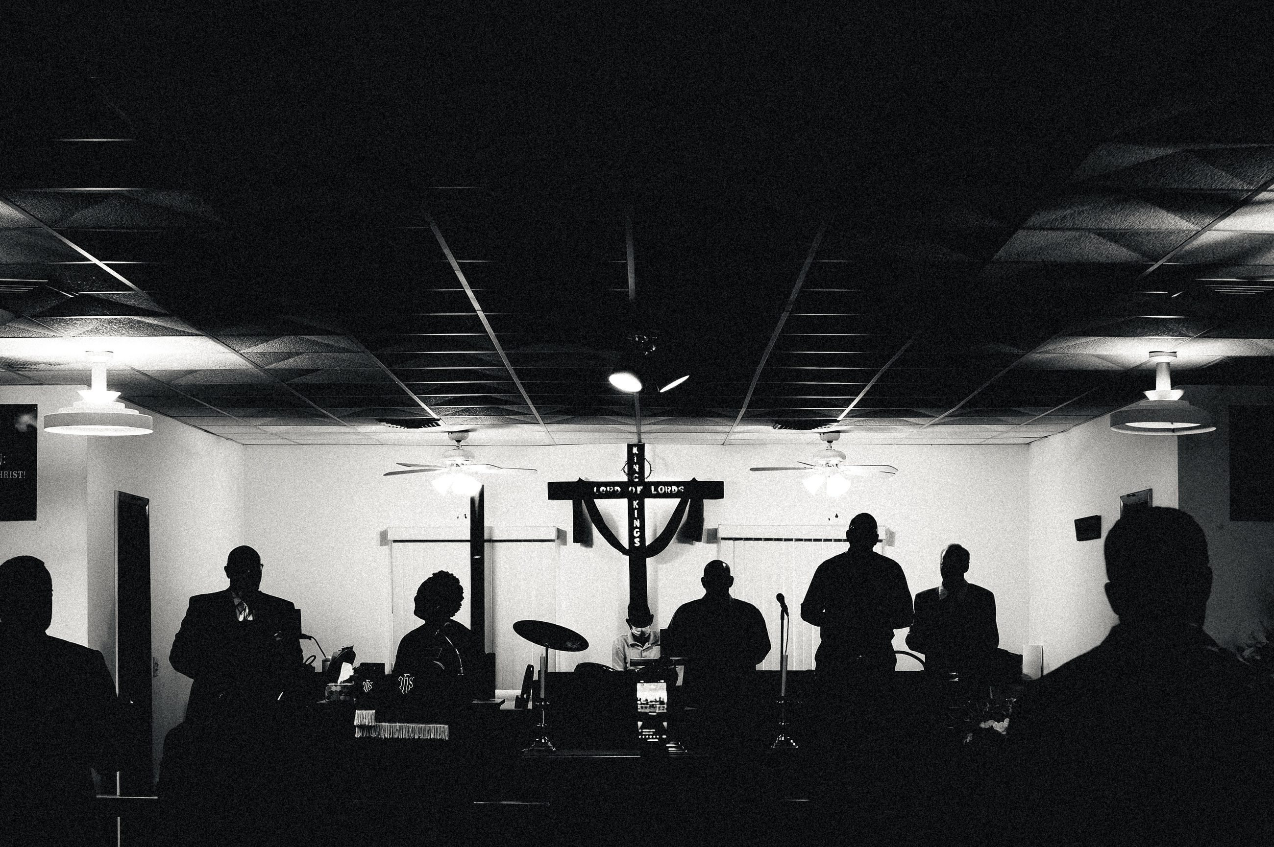 The congregation seen from the back of the small church, silhouetted, a draped cross at the front.