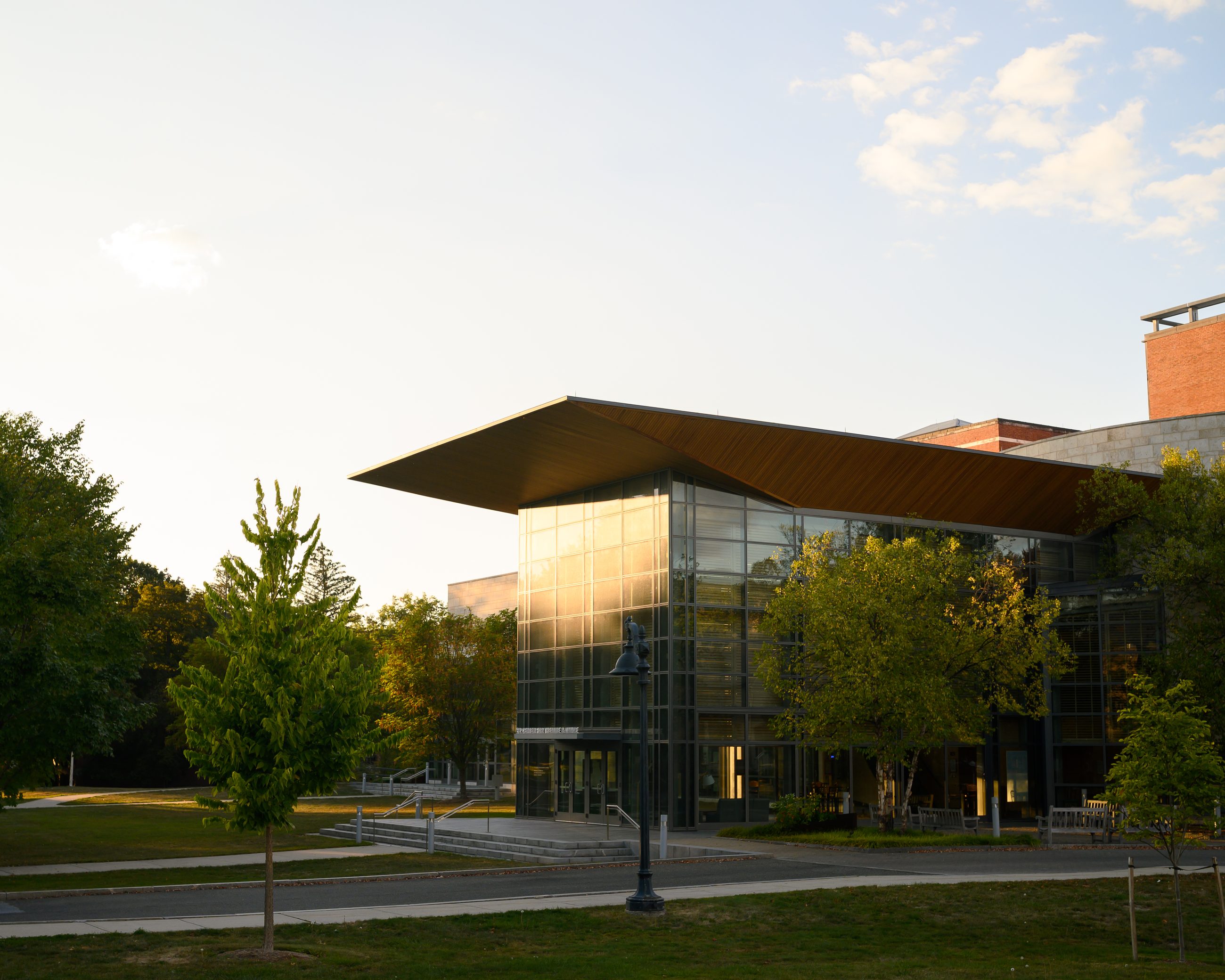 The same building from the lawn, its cantilevered roof running out over glass, late sun on the grass.