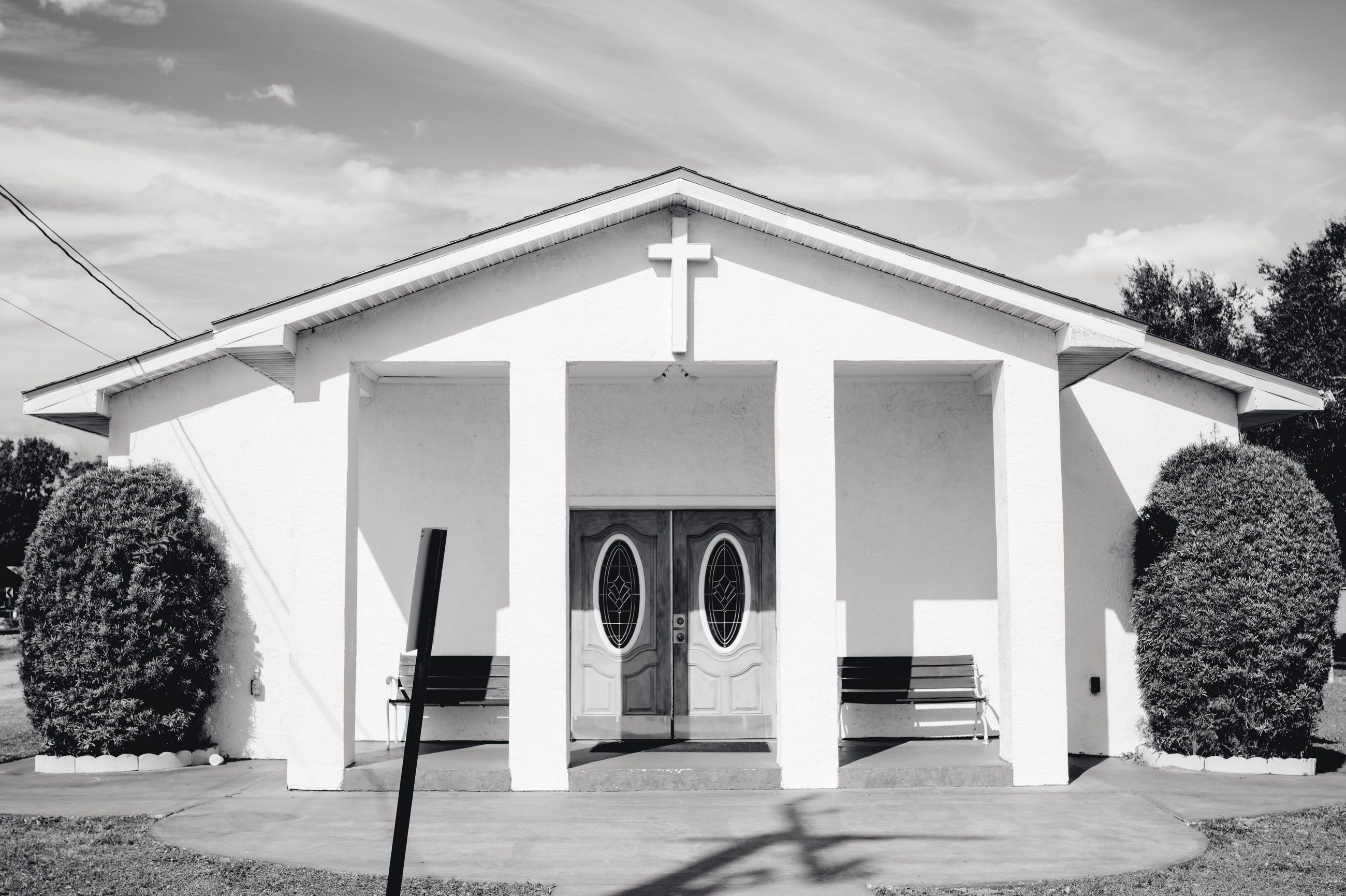 The white front of the chapel, columns either side of the doors, bushes at the steps.