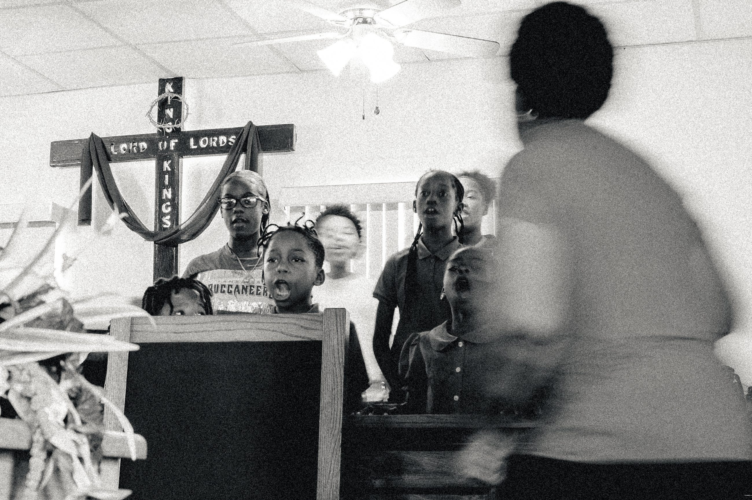 Children gathered behind the pulpit, a figure crossing the frame in front of them.