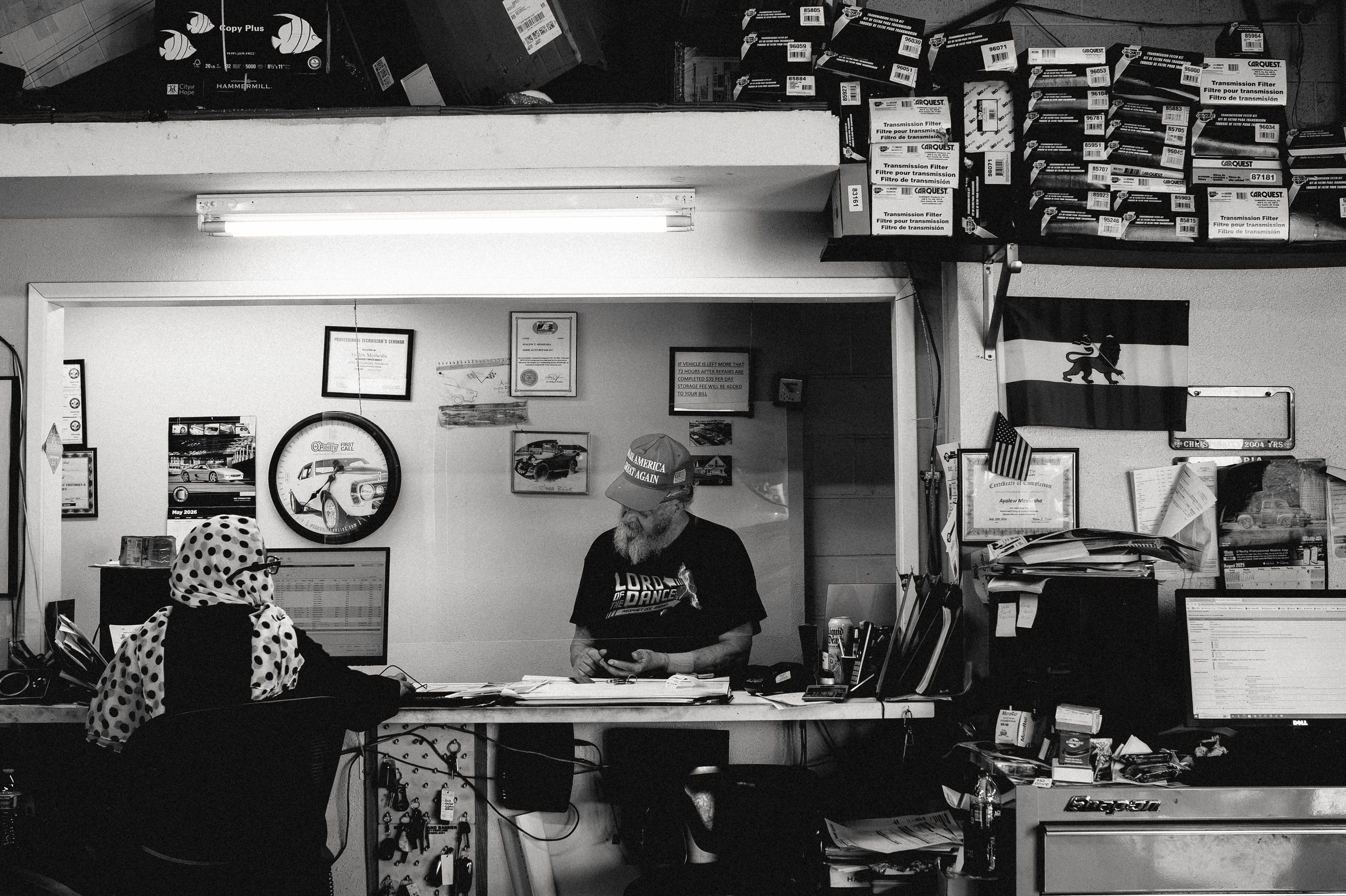 A man working at the counter of the shop office, the walls behind him covered in notices and framed certificates.