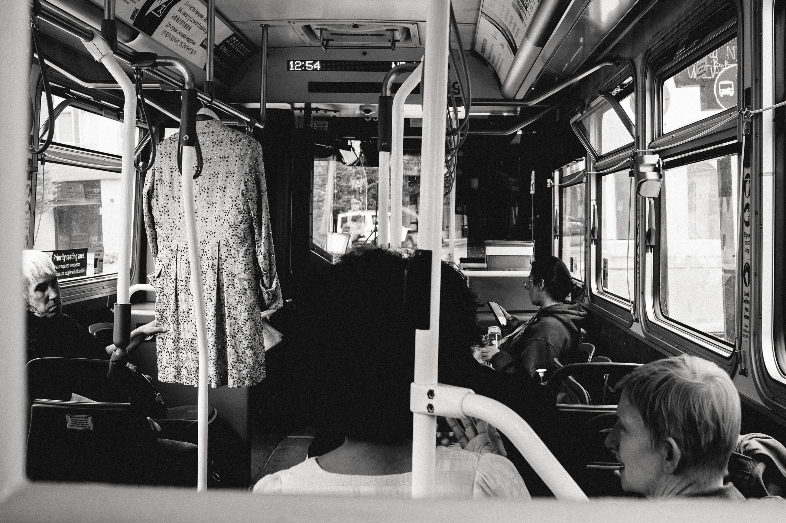 The inside of a city bus in motion, passengers seated along the windows, hand rails overhead.