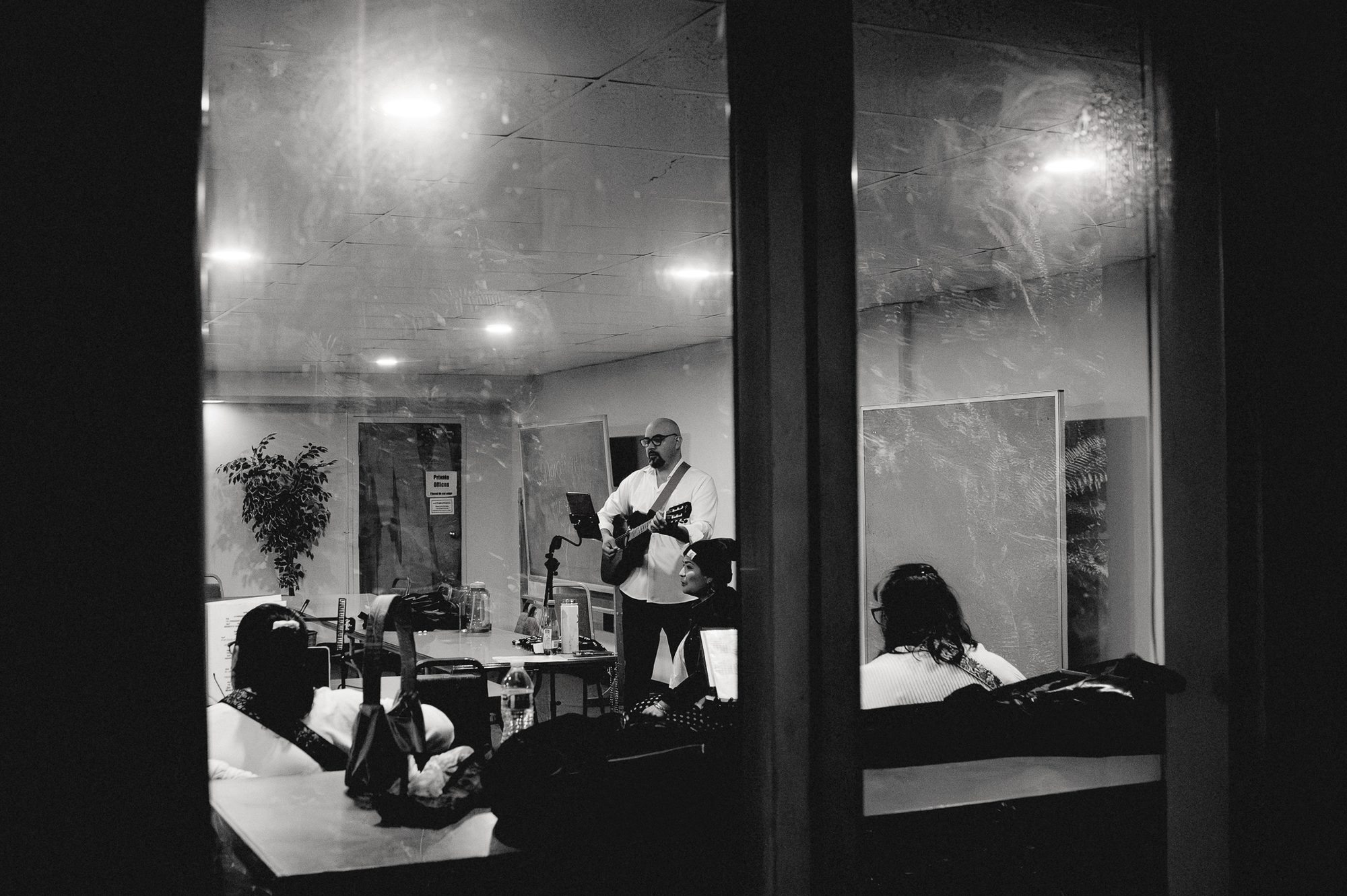 A lit shopfront seen from the street at night, people gathered on the floor inside.