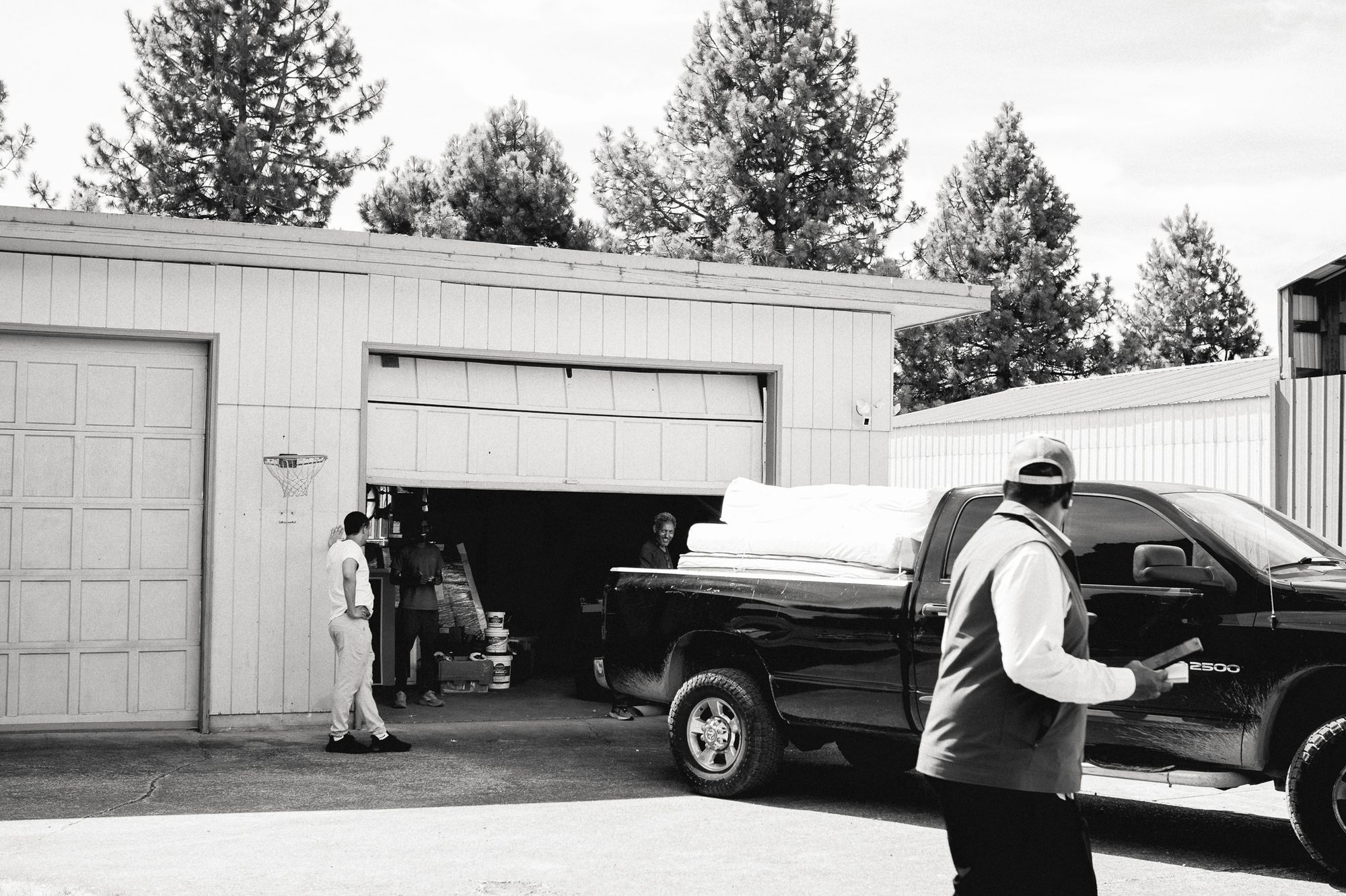 An open garage on a residential street, a pickup truck backed in, two men and a child around it.